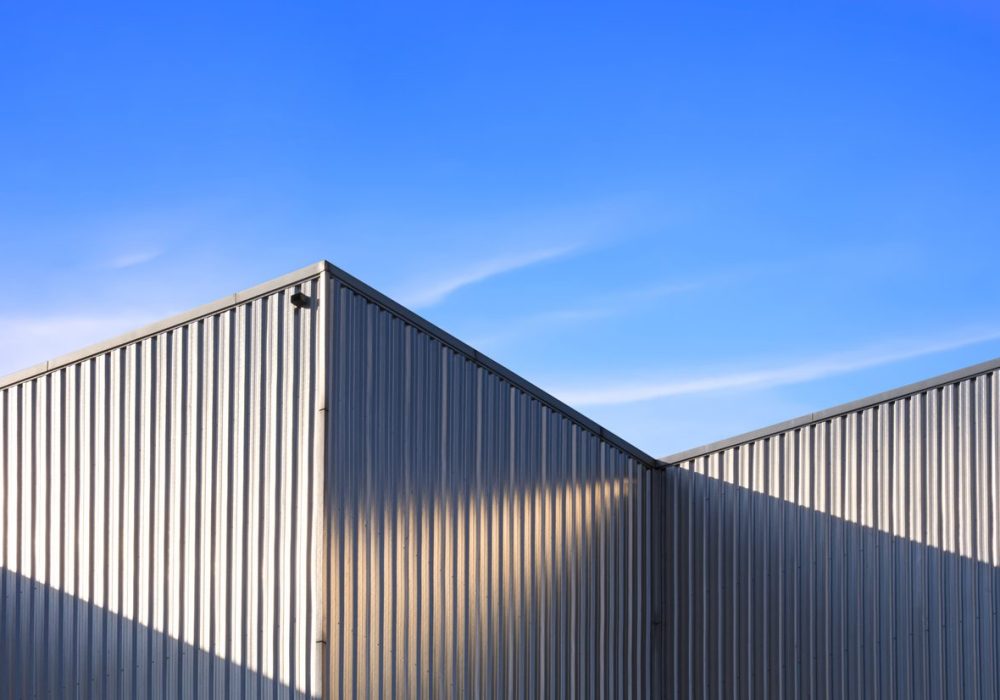 Corrugated Steel Wall of industrial Warehouse Building against blue sky background with sunlight and shadow on surface